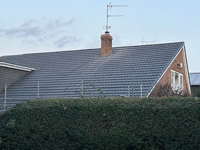 A brick chimney stack rising from a grey pantile roof