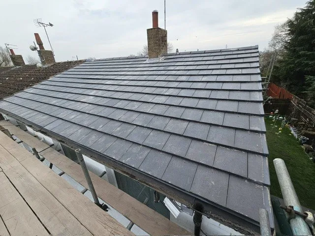 A slope of dark grey slates seen from the scaffold, with a gutter along the eaves