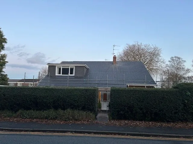 A grey pantile roof with a dormer window on a house beside a tall hedge
