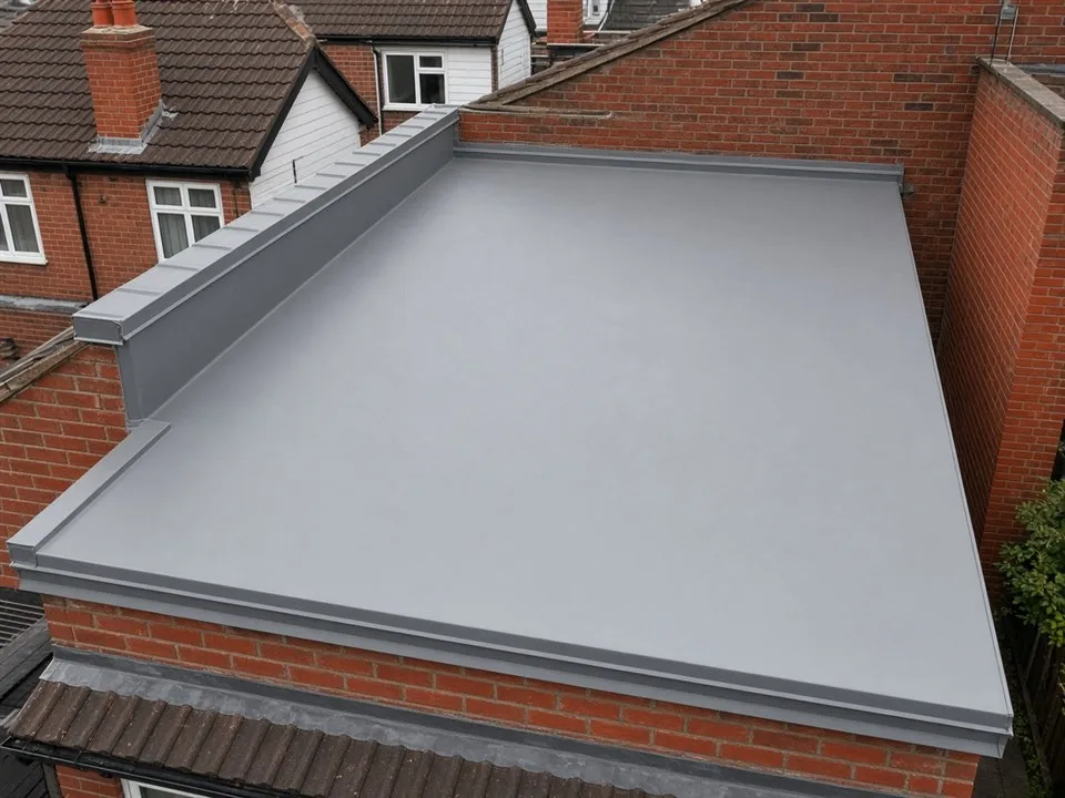 A finished grey fibreglass flat roof, with the edge trim and the upstand against the brick wall