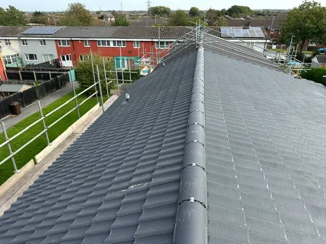 A dry-fixed ridge running along a new grey tiled roof, with scaffold at the eaves