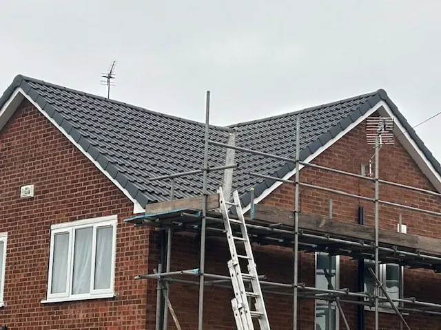A new grey pantile roof on a red-brick house, with white bargeboards and scaffold still in place
