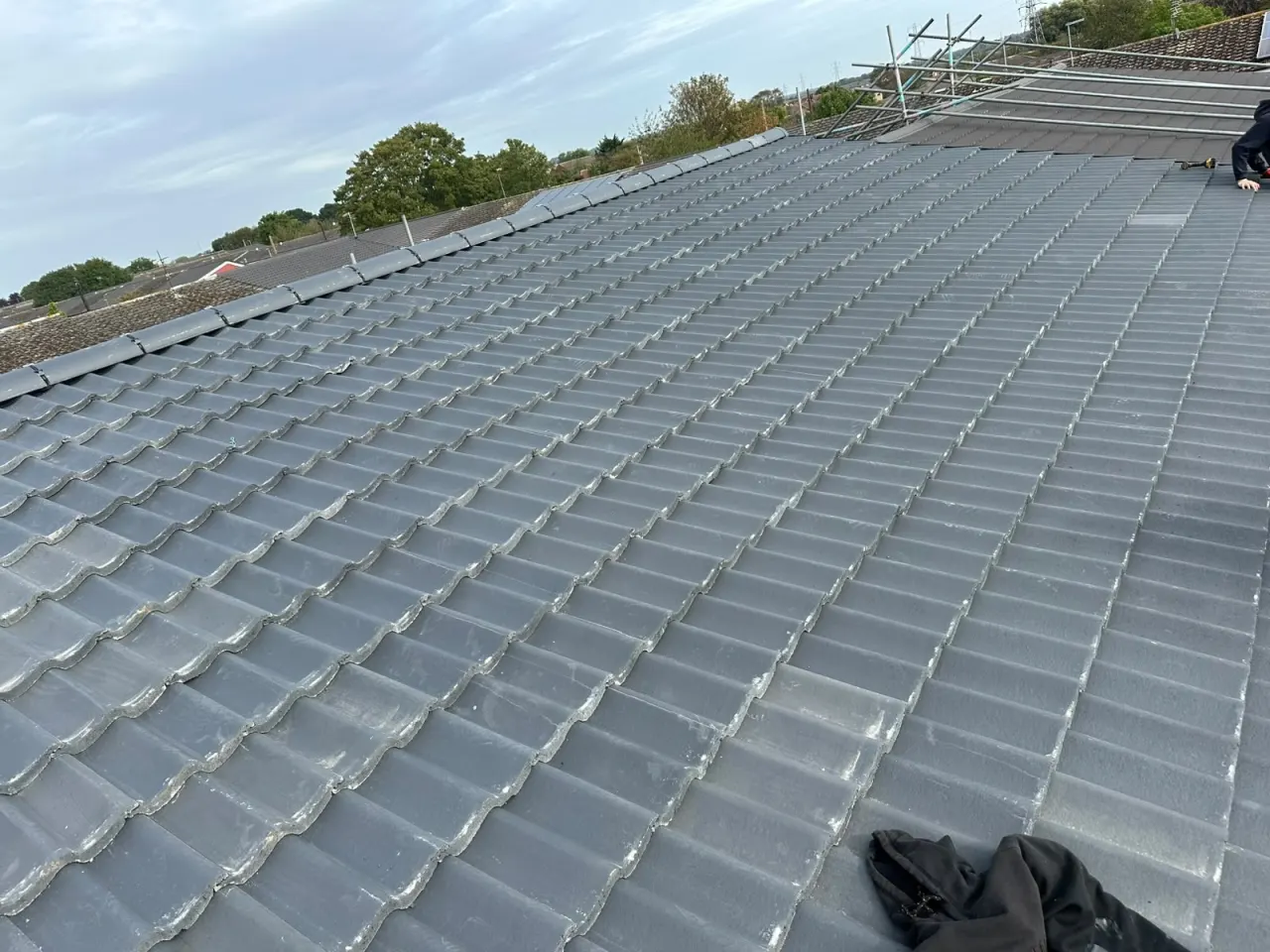 Grey concrete interlocking tiles being laid in courses across a roof